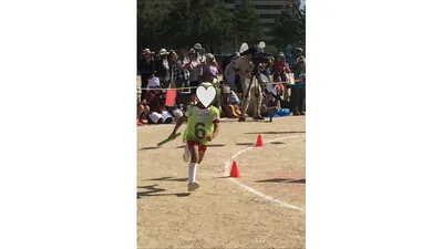 ゼッケンをつけてバトンを握り、かけっこでコーナーを走る子ども