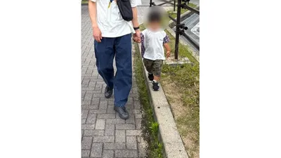 大人と手をつなぎ、縁石の上をバランスをとって歩く子ども