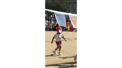 赤い帽子をかぶり、園庭のトラックを力いっぱい走る子ども