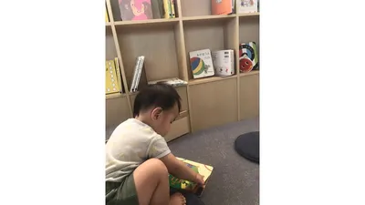 本棚の前で絵本を開く1歳の息子